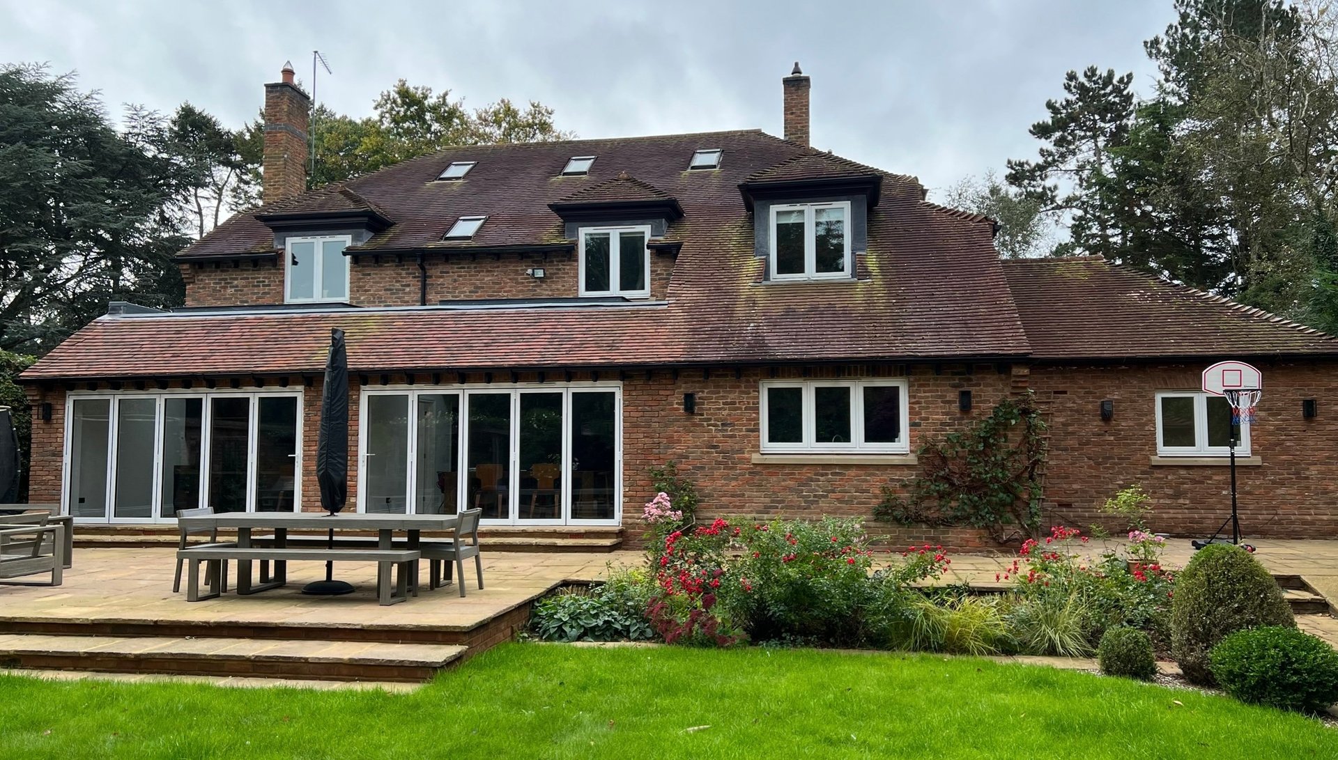 Modern brick house with large glass extension, wooden deck, manicured garden and lawn