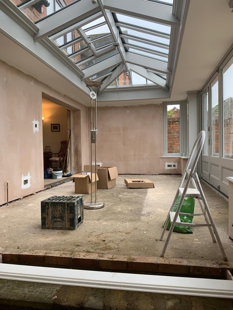Interior of home renovation in progress showing empty room with skylight, glass roof panels, cardboard boxes, ladder, and exposed walls