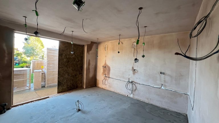 Empty room under renovation with blue floor, drywall, exposed wiring, and open door to patio