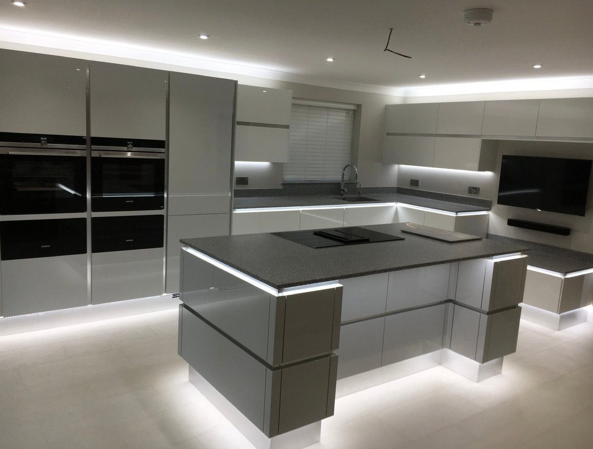 Modern kitchen with grey and white cabinetry, illuminated central island with cooktop, stainless steel appliances, and LED lighting throughout
