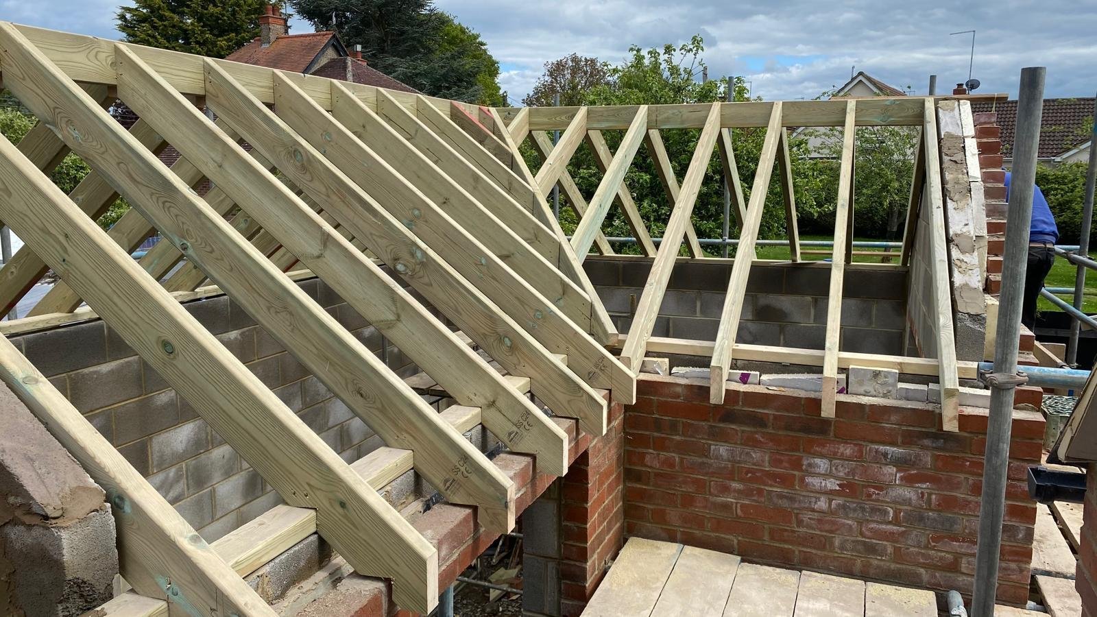 Wooden roof trusses and rafters under construction on a brick building frame with open sky visible