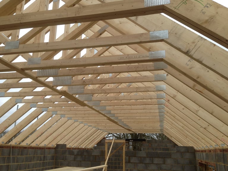Interior view of a wooden roof frame under construction with exposed timber beams and corrugated panels