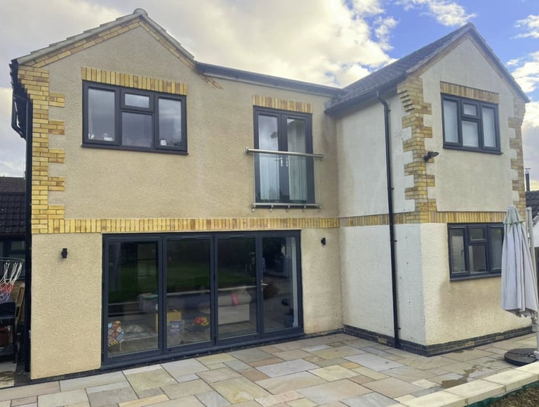 Modern two-story residential house with cream and yellow brick exterior, black-framed windows, and a dark ground floor garage or extension.