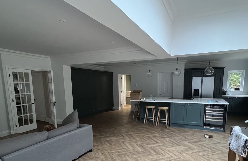 Modern open-concept living space with kitchen island, gray cabinetry, herringbone flooring, and contemporary lighting fixtures