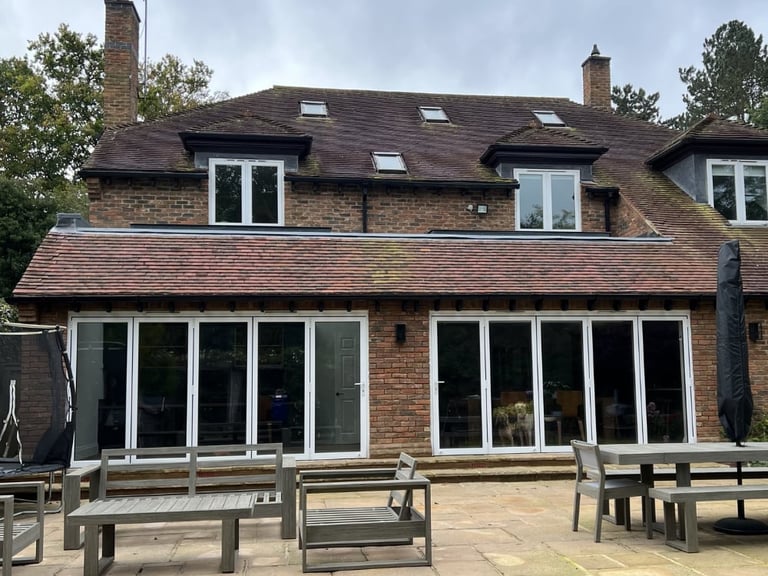 Modern brick house with multi-pane windows, extended patio area, and outdoor seating under cloudy sky